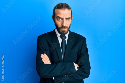 Attractive man with long hair and beard wearing business suit and tie skeptic and nervous, disapproving expression on face with crossed arms. negative person.