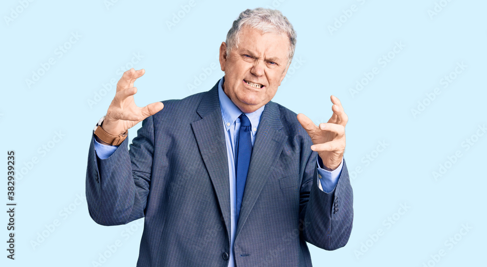 Senior grey-haired man wearing business jacket shouting frustrated with rage, hands trying to strangle, yelling mad