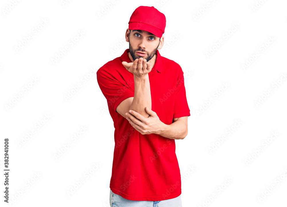 Young handsome man with beard wearing delivery uniform looking at the camera blowing a kiss with hand on air being lovely and sexy. love expression. Young handsome man with beard wearing delivery uniform looking at the camera blowing a kiss with hand on air being lovely and sexy. love expression.
