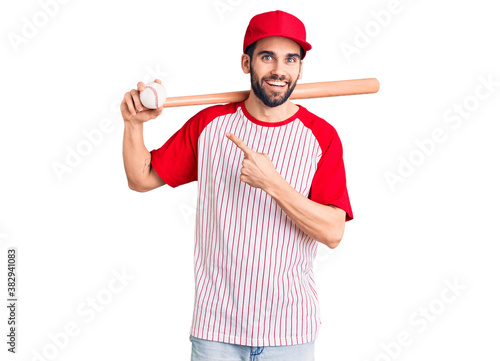 Young handsome man with beard playing baseball holding bat and ball smiling happy pointing with hand and finger