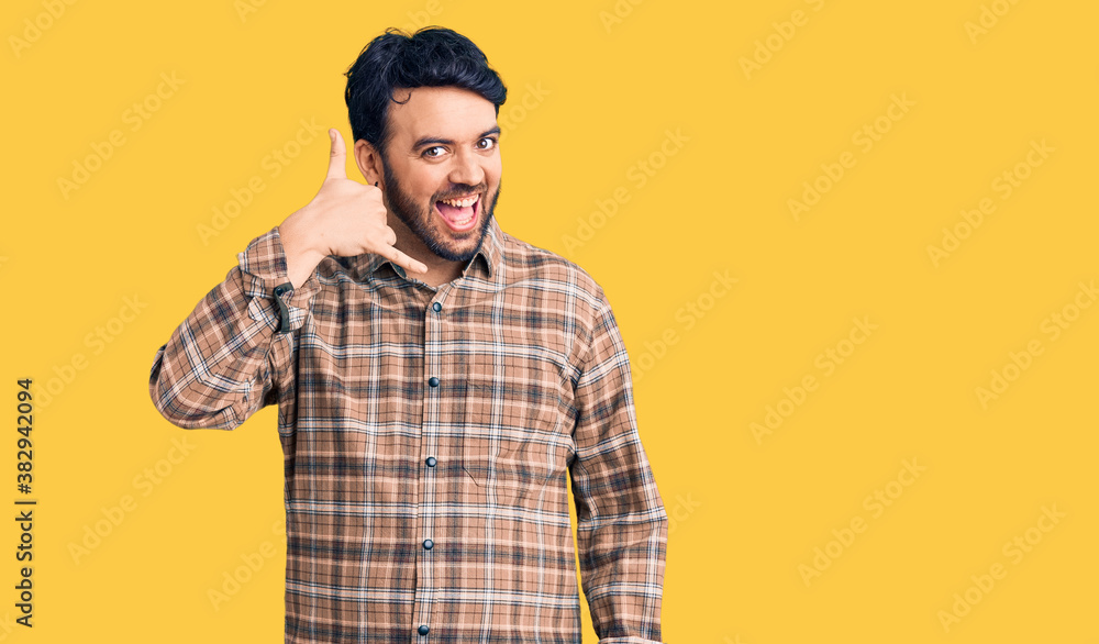 Young hispanic man wearing casual clothes smiling doing phone gesture with hand and fingers like talking on the telephone. communicating concepts. Young hispanic man wearing casual clothes smiling doing phone gesture with hand and fingers like talking on the telephone. communicating concepts.