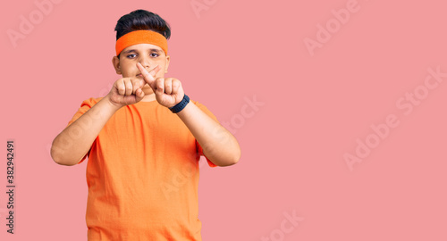 Little boy kid wearing sportswear rejection expression crossing fingers doing negative sign