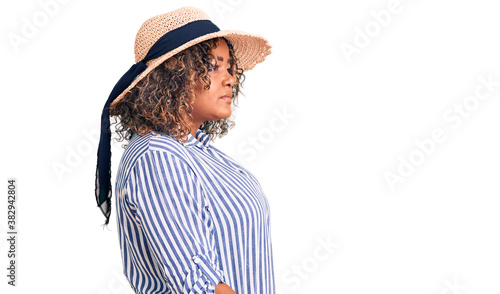 Young african american plus size woman wearing summer hat looking to side, relax profile pose with natural face with confident smile.