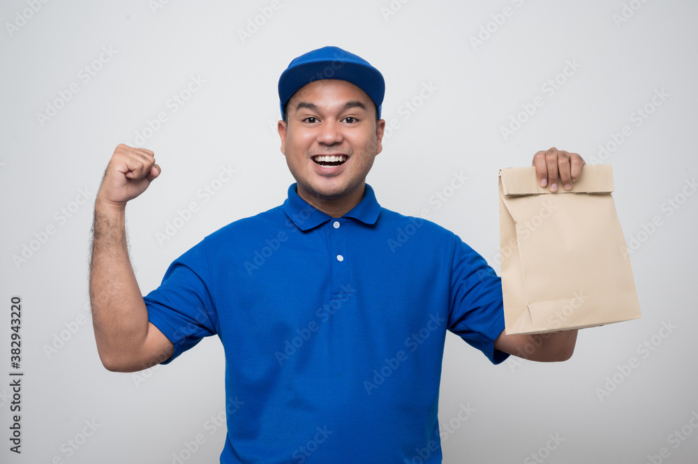 Young smiling asian delivery man in blue uniform holding paper bag food delivery on isolated white background..
