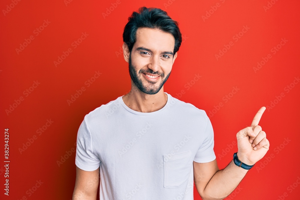 Young hispanic man wearing casual white tshirt with a big smile on face, pointing with hand finger to the side looking at the camera. Young hispanic man wearing casual white tshirt with a big smile on face, pointing with hand finger to the side looking at the camera.