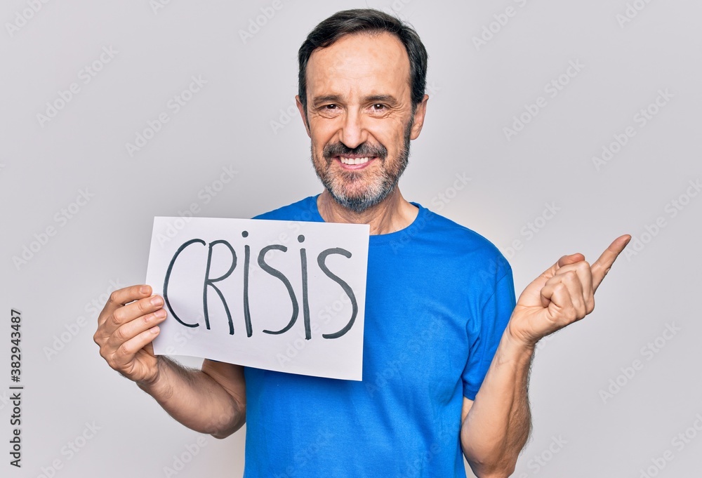 Middle age handsome man holding paper with crisis message over isolated white background smiling happy pointing with hand and finger to the side Middle age handsome man holding paper with crisis message over isolated white background smiling happy pointing with hand and finger to the side