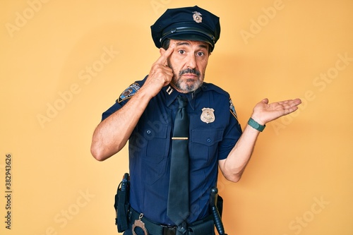 Canvas-taulu Middle age hispanic man wearing police uniform confused and annoyed with open palm showing copy space and pointing finger to forehead
