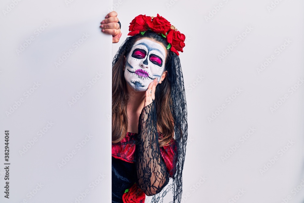 Young woman wearing day of the dead custome holding blank empty banner touching mouth with hand with painful expression because of toothache or dental illness on teeth. dentist concept. Young woman wearing day of the dead custome holding blank empty banner touching mouth with hand with painful expression because of toothache or dental illness on teeth. dentist concept.