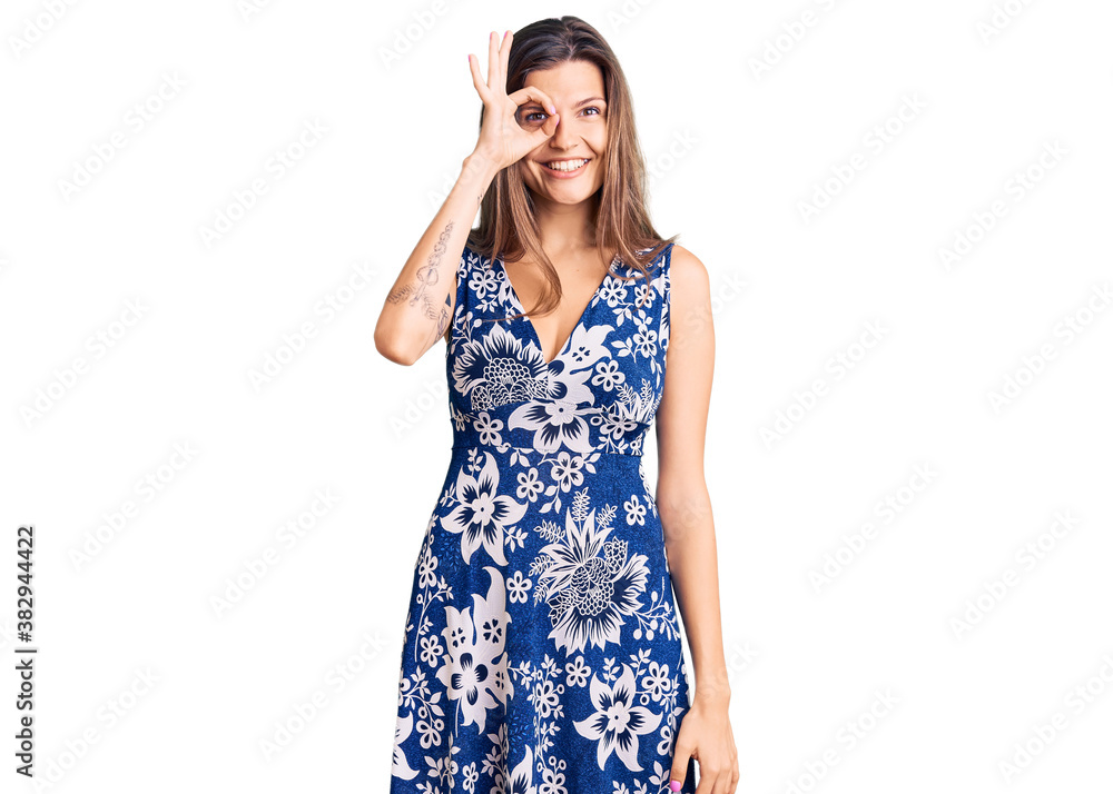 Beautiful caucasian woman wearing summer dress doing ok gesture with hand smiling, eye looking through fingers with happy face. Beautiful caucasian woman wearing summer dress doing ok gesture with hand smiling, eye looking through fingers with happy face.