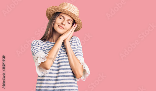 Beautiful caucasian woman wearing summer hat sleeping tired dreaming and posing with hands together while smiling with closed eyes.