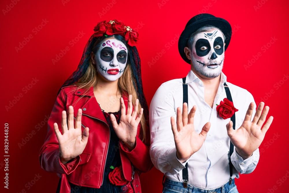 Couple wearing day of the dead costume over red moving away hands palms showing refusal and denial with afraid and disgusting expression. stop and forbidden. Couple wearing day of the dead costume over red moving away hands palms showing refusal and denial with afraid and disgusting expression. stop and forbidden.