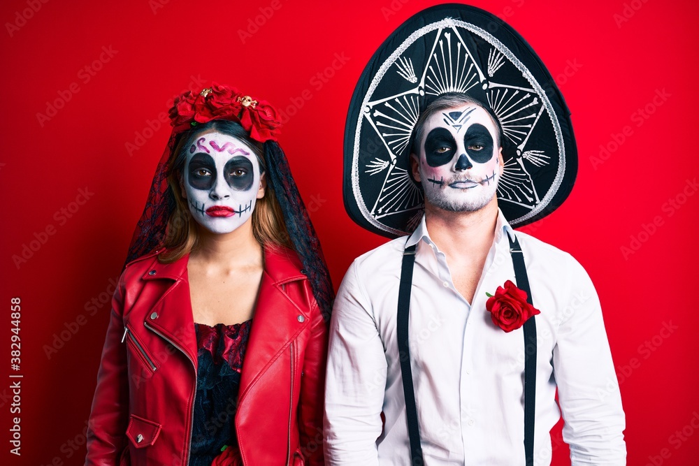Couple wearing day of the dead costume over red with serious expression on face. simple and natural looking at the camera. Couple wearing day of the dead costume over red with serious expression on face. simple and natural looking at the camera.