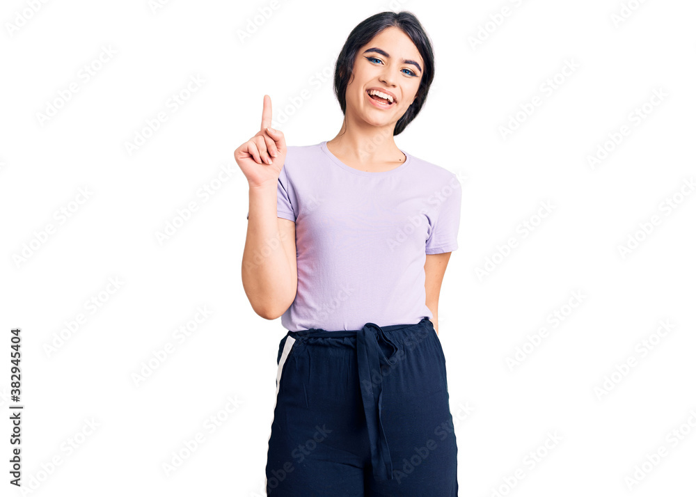 Brunette teenager girl wearing casual clothes showing and pointing up with finger number one while smiling confident and happy. Brunette teenager girl wearing casual clothes showing and pointing up with finger number one while smiling confident and happy.