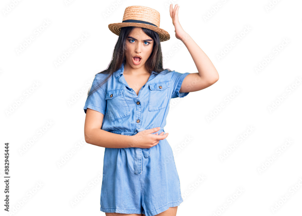 Brunette teenager girl wearing summer hat surprised with hand on head for mistake, remember error. forgot, bad memory concept. Brunette teenager girl wearing summer hat surprised with hand on head for mistake, remember error. forgot, bad memory concept.