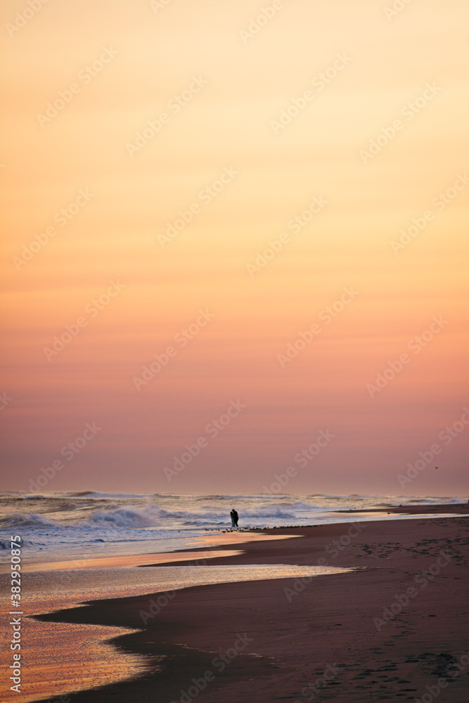 Couple holding each other close on the beach as waves break during sunset