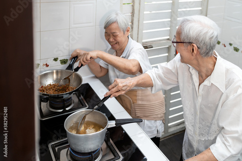 Fototapeta Naklejka Na Ścianę i Meble -  Happy smiling asian senior women are cooking stir-fried pork with basil and soup,elderly siblings enjoying preparing meal Thai food in kitchen at home,healthy food,concoction,family lifestyle concept