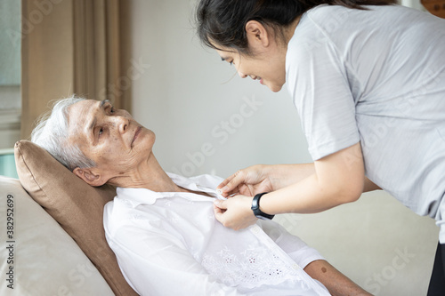 Tableau sur toile Asian female caregiver taking care of helping elderly patient get dressed,button