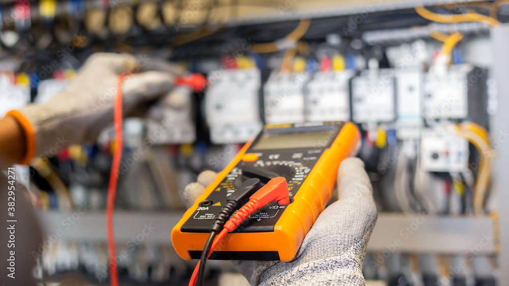 Fototapeta premium Electrician engineer uses a multimeter to test the electrical installation and power line current in an electrical system control cabinet.