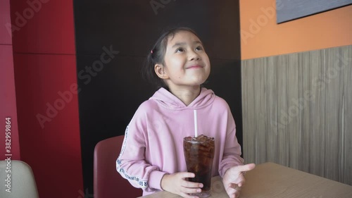 Asian little girl drinking a glass of refreshing cold fizzy cola drink with smile face.