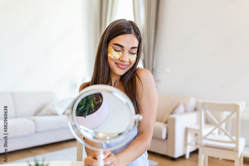 Portrait of pretty, nice young woman with golden eye patches, having bags under eyes in the morning because of less sleep, showing an effect of perfect skin. Looking in the mirror Portrait of pretty, nice young woman with golden eye patches, having bags under eyes in the morning because of less sleep, showing an effect of perfect skin. Looking in the mirror