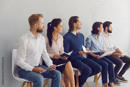 Young candidates sitting in row on chairs waiting for job interview in modern business company