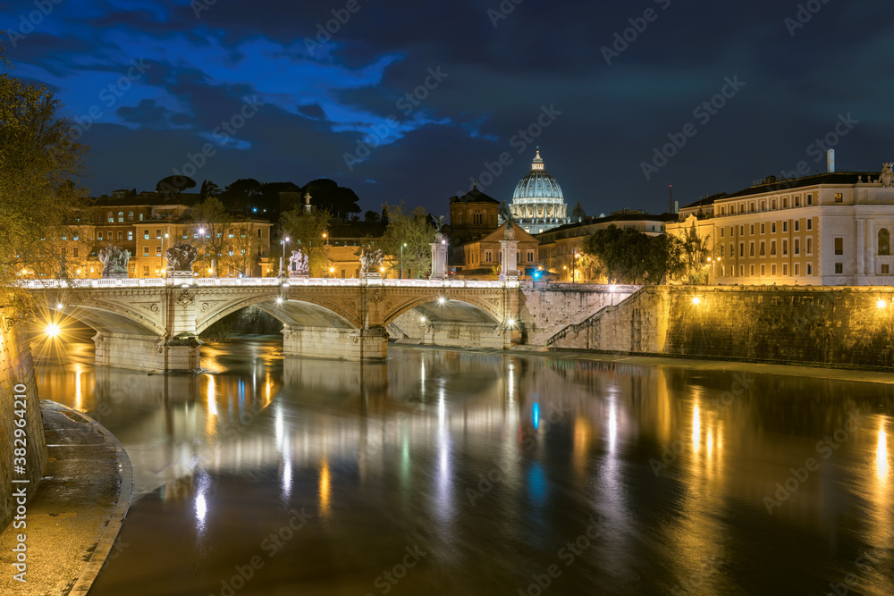 Rome at night, Italy. Dome of Saint Peter Basilica in Vatican city and Sant Angelo Bridge, reflection on Tiber river at night in Rome, Italy.