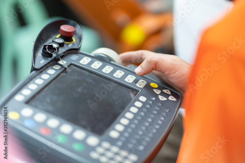 Man is holding a teach pendant to control a robot arm that is integrated into a smart factory production line. automation line which is equipped with sensors and robot arm. Selective Focus.
