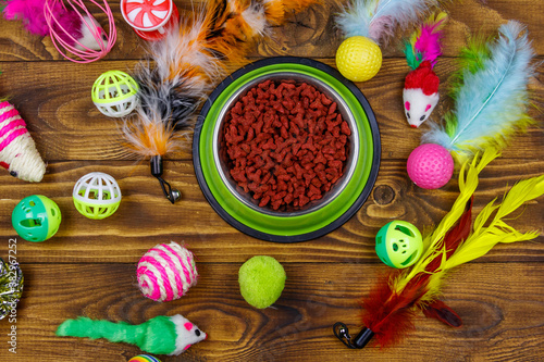 Set of toys for cat and bowl with dry pet food on wooden background. Top view. Pet care concept