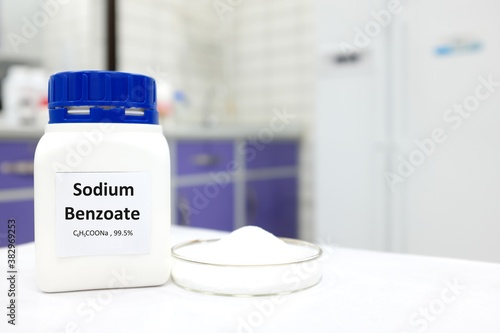 Selective focus of bottle of pure sodium benzoate food additive beside a petri dish with white solid powder substance. White laboratory background with copy space. photo
