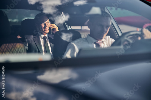 Smiling businessman with smartphone travelling with chauffeur photo
