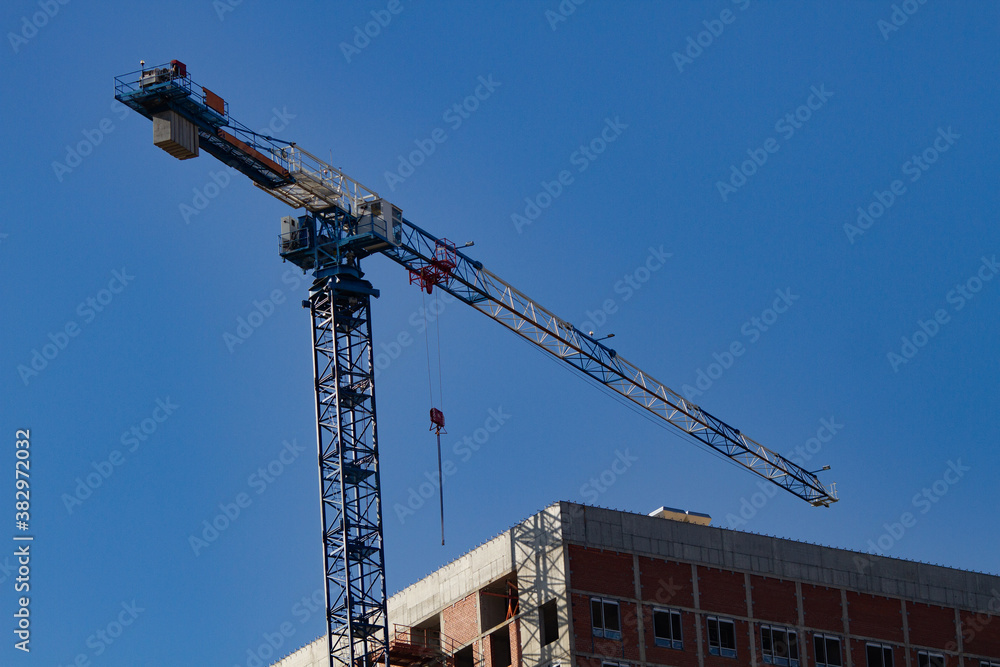 Construction concept: a crane building a multi-storey building against a blue background. Modern buildings.
