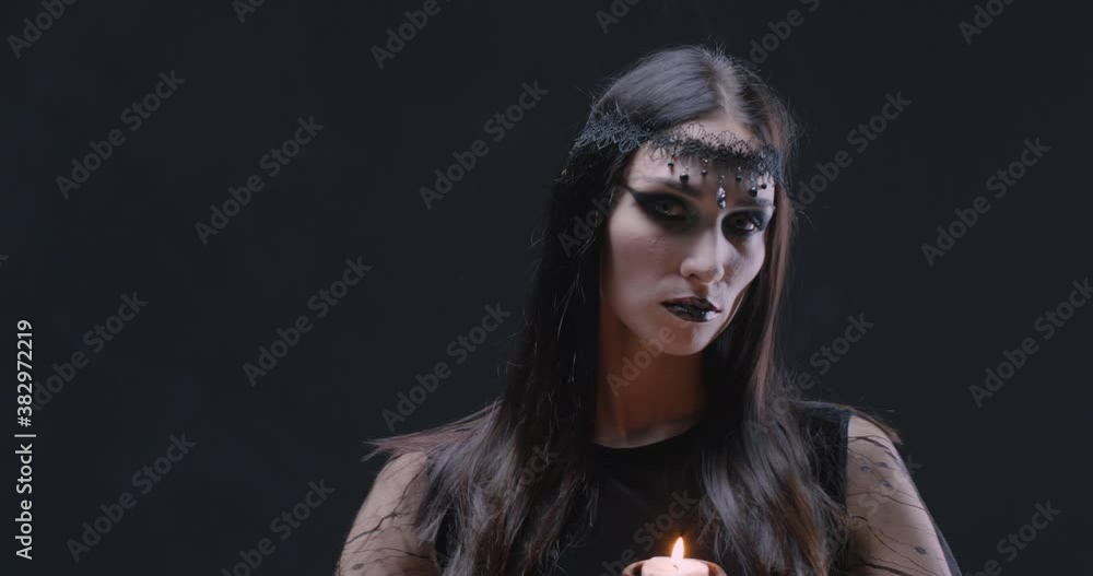 Mystical female in black attire holds a skull with a burning candle and looking at the camera, the celebration of Halloween, portrait of a beautiful young woman. Mystical female in black attire holds a skull with a burning candle and looking at the camera, the celebration of Halloween, portrait of a beautiful young woman.