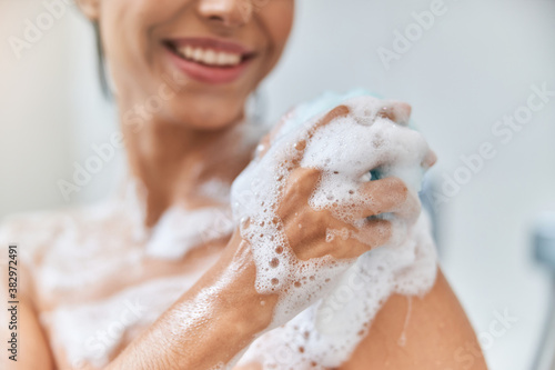 Cheerful young woman washing her body with bath loofah