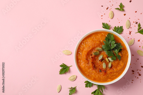 Composition with bowl of pumpkin soup on pink background, top view