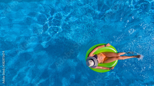 Beautiful woman in hat in swimming pool aerial view from above, young girl in bikini relaxes and swims on inflatable ring donut and has fun in water on vacation
