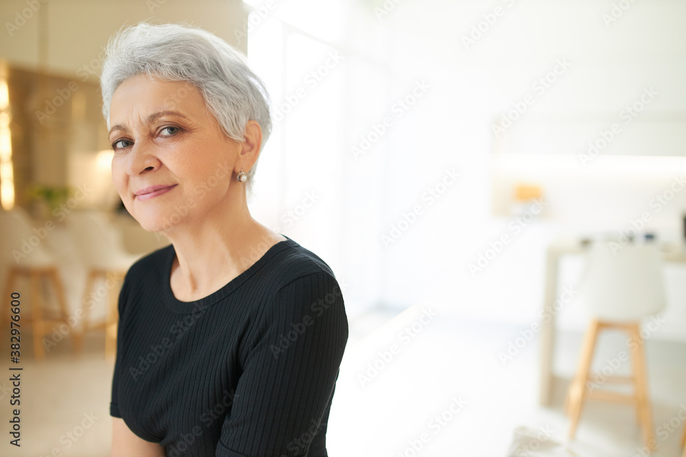 Beauty, femininity, style and aging concept. Half profile of adorable joyful middle aged female pensioner with gray short haircut posing indoors in black t-shirt, having relaxed pleased look Beauty, femininity, style and aging concept. Half profile of adorable joyful middle aged female pensioner with gray short haircut posing indoors in black t-shirt, having relaxed pleased look
