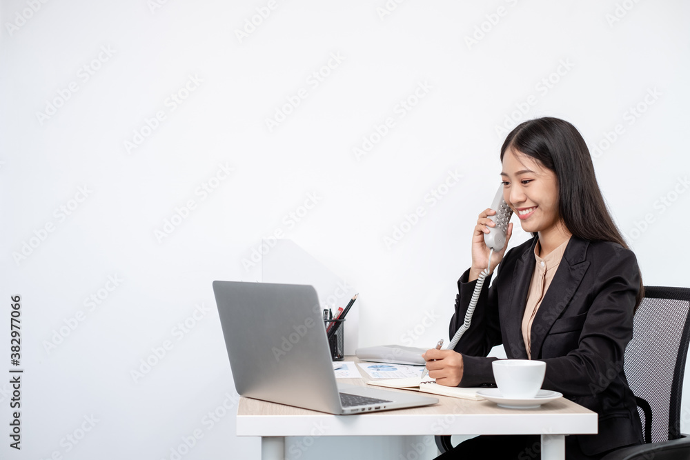Asian businesswoman talking on the phone and working on a laptop with a cheerful and happy smile while working at the office Asian businesswoman talking on the phone and working on a laptop with a cheerful and happy smile while working at the office