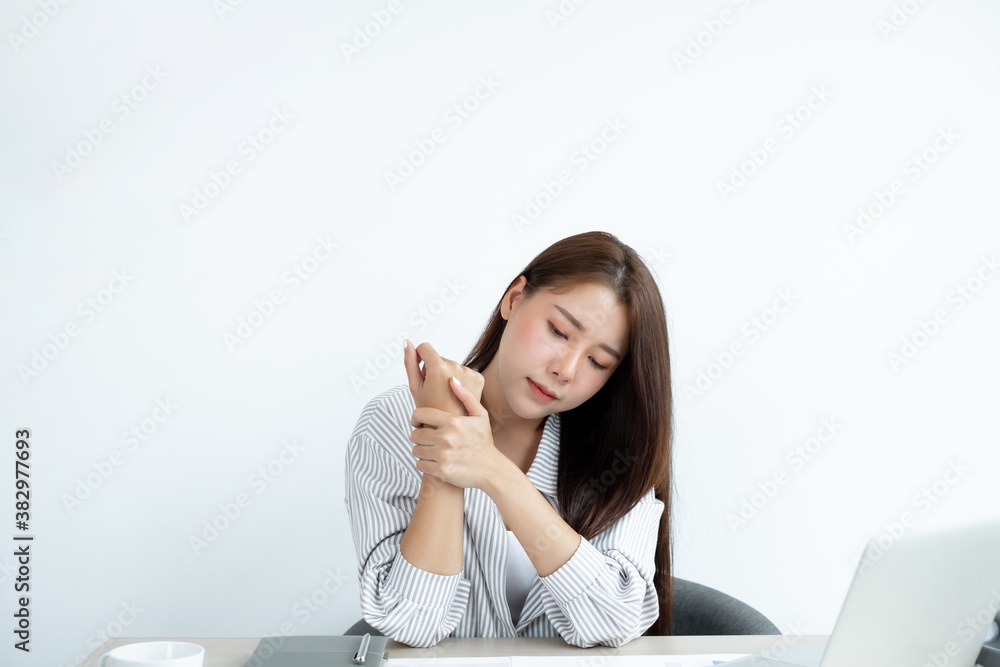 An Asian woman is sitting overtime with her laptop and her wrist aches while working at the office An Asian woman is sitting overtime with her laptop and her wrist aches while working at the office