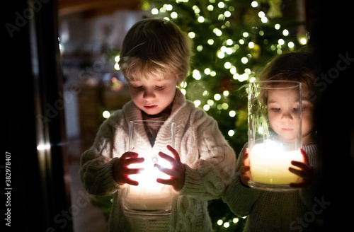 Portrait of small girl and boy indoors at home at Christmas, holding candles. photo