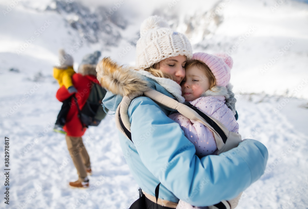 Mother with happy small daughter in carrier standing in winter nature, resting.