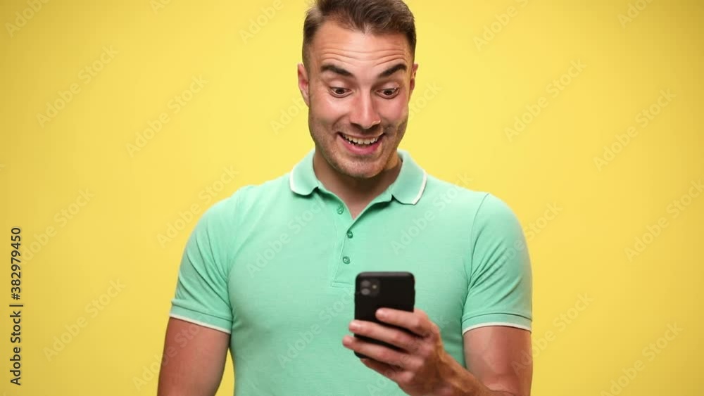 attractive casual man texting on his mobile phone, being happily surprised then excited, celebrating succes on yellow background attractive casual man texting on his mobile phone, being happily surprised then excited, celebrating succes on yellow background