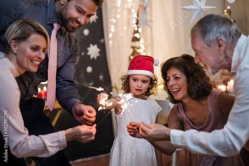 Small girl with parents and grandparents indoors celebrating Christmas  holding sparklers.