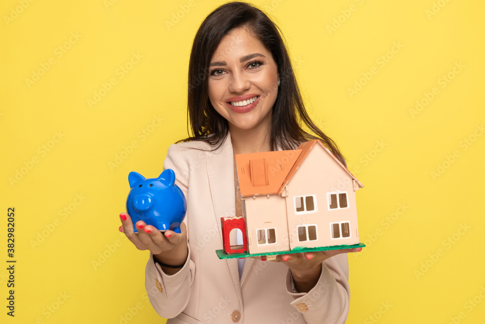 happy young woman showing piggy bank and building model happy young woman showing piggy bank and building model