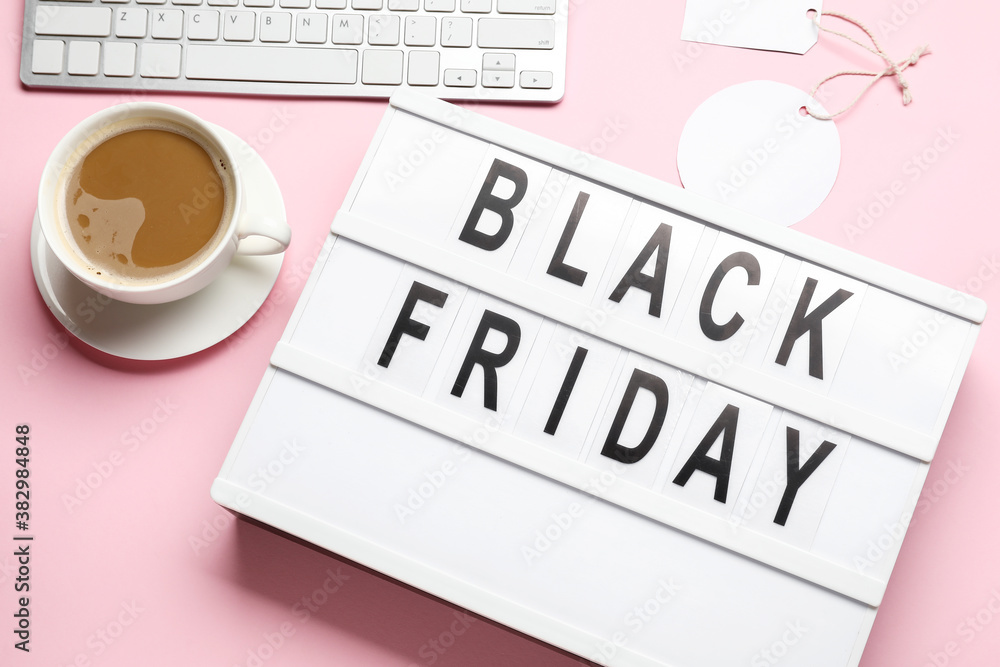 Board with text BLACK FRIDAY, cup of coffee and computer on color background Board with text BLACK FRIDAY, cup of coffee and computer on color background