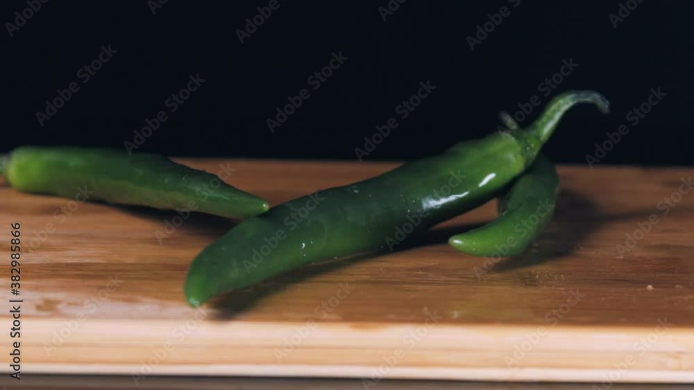 Green chilli pepper and wooden board in slow motion. Pepper falling on a wooden table. Falling vegetables in slow motion. Green chilli pepper and wooden board in slow motion. Pepper falling on a wooden table. Falling vegetables in slow motion.