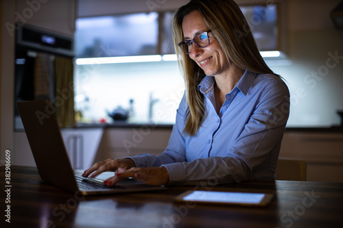 Pretty, middle-aged woman working late in the day on a laptop computer at home, running a business from home