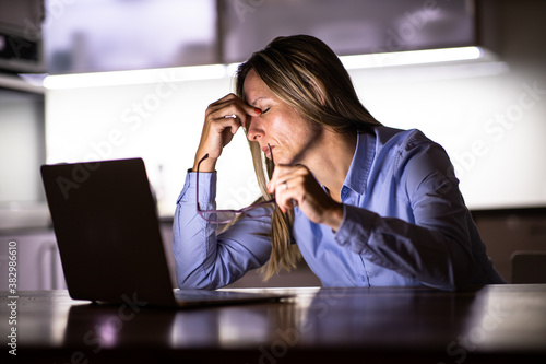 Pretty, middle-aged woman working late in the day on a laptop computer at home, running a business from home/working remotely - getting frustrated photo