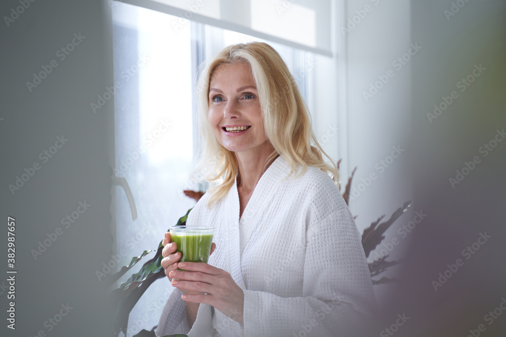 Smiling blonde lady standing with glass of healthy drink Smiling blonde lady standing with glass of healthy drink
