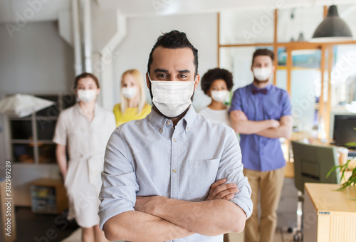 business  health and people concept - young man with beard over creative team wearing face protective medical mask for protection from virus disease at office