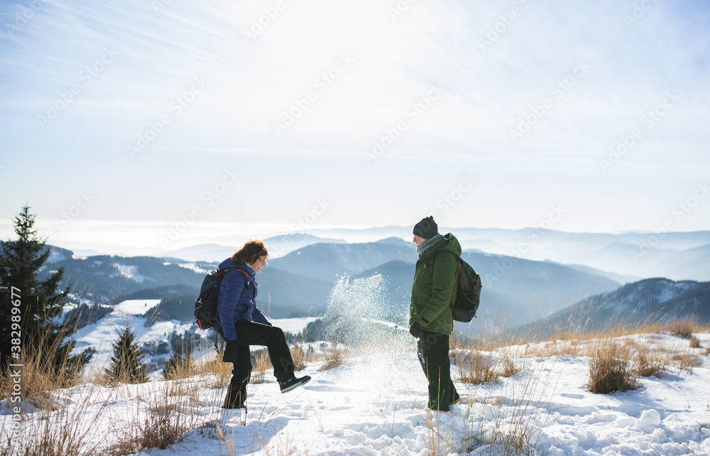 Side view of senior couple hikers standing in snow-covered winter nature.